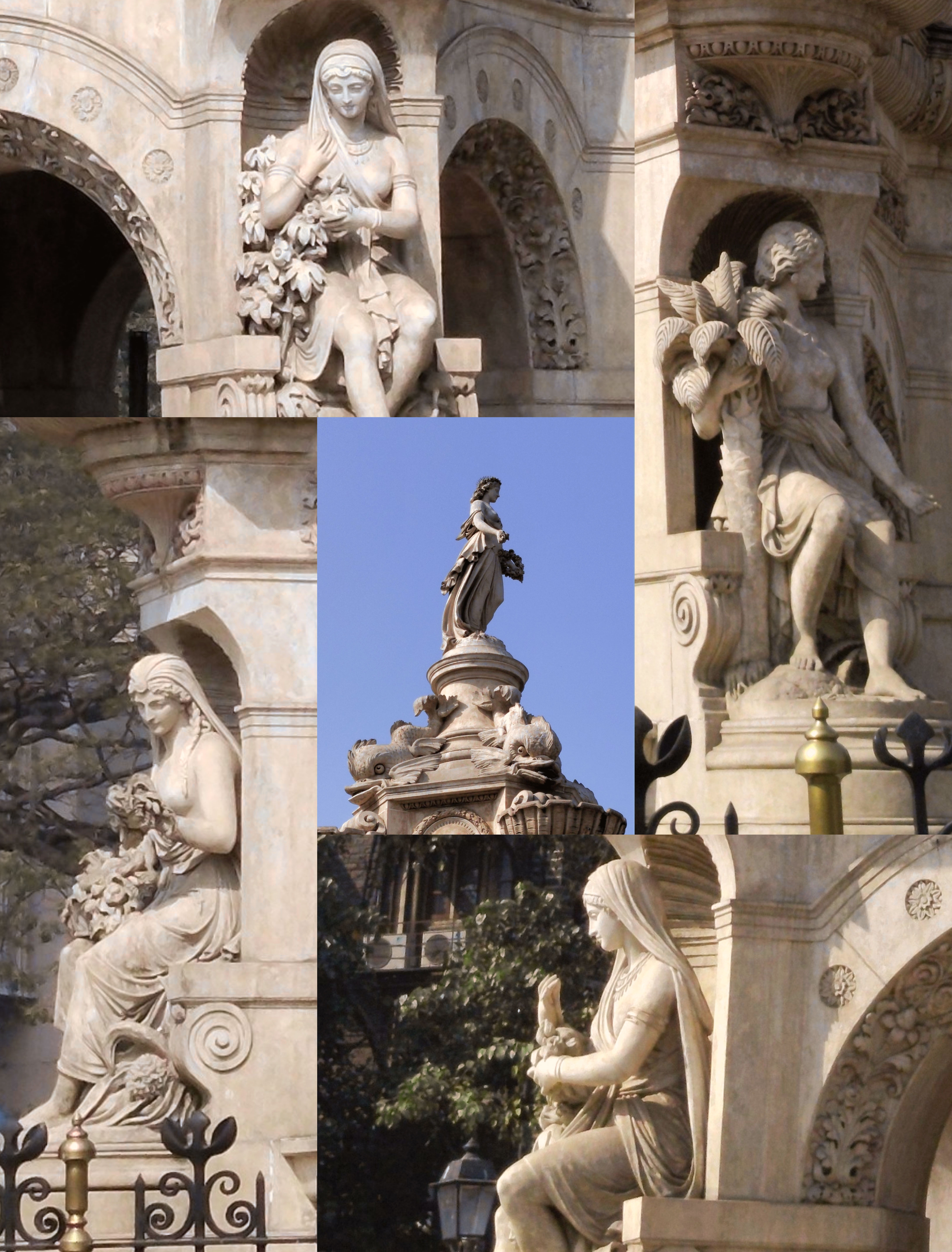 A collage of statues on an ornate stone monument, featuring various seated figures and a standing figure at the top against a blue sky background.